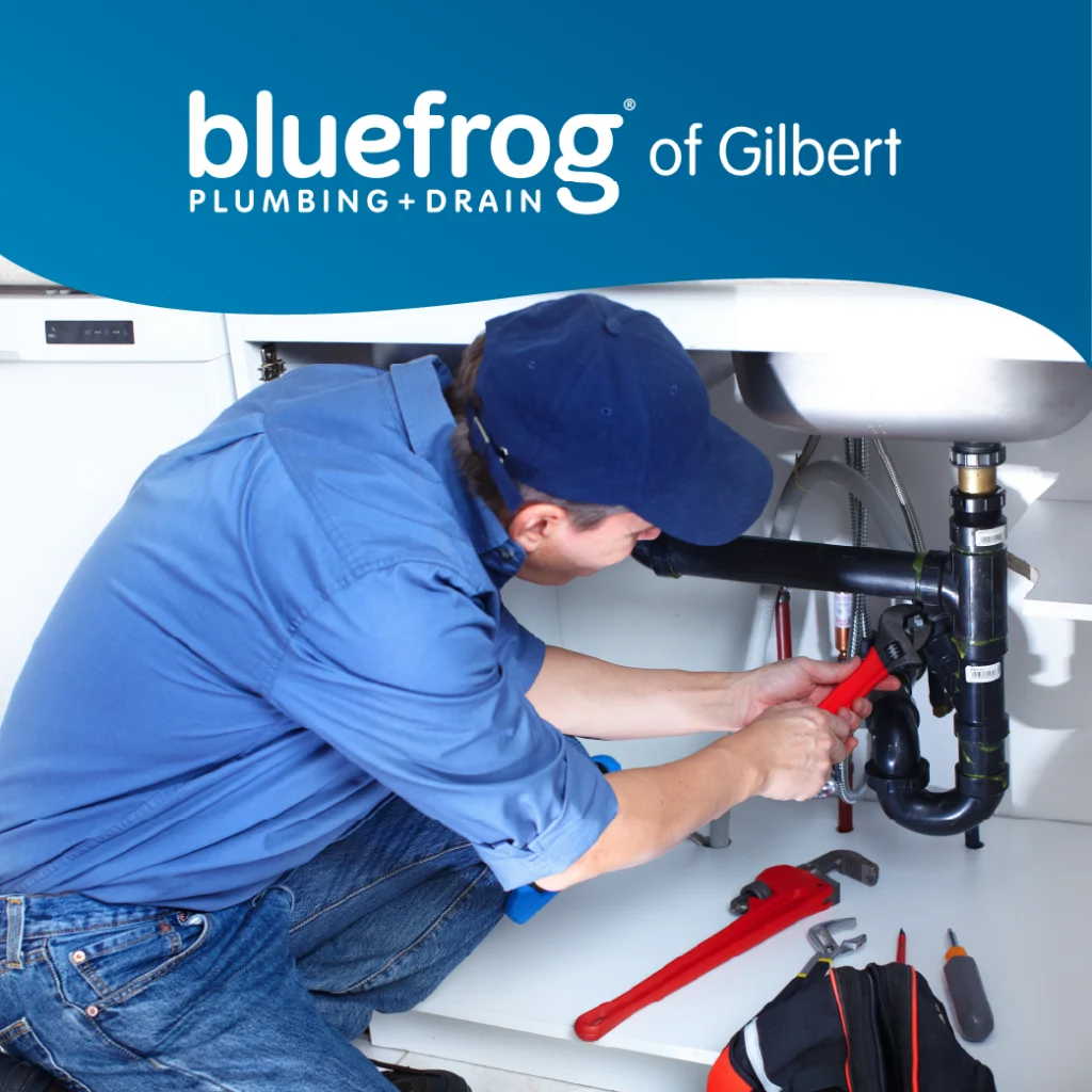 Technician crouched under a sink using a red pipe wrench on dark plumbing fixtures